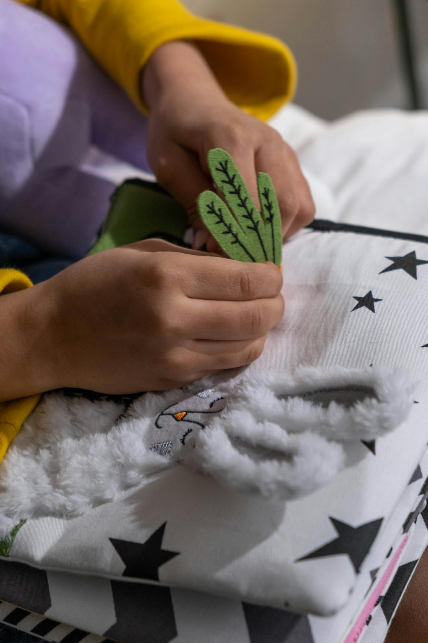 Close-up of hands crafting a handmade embroidered textile with star patterns and felt elements.