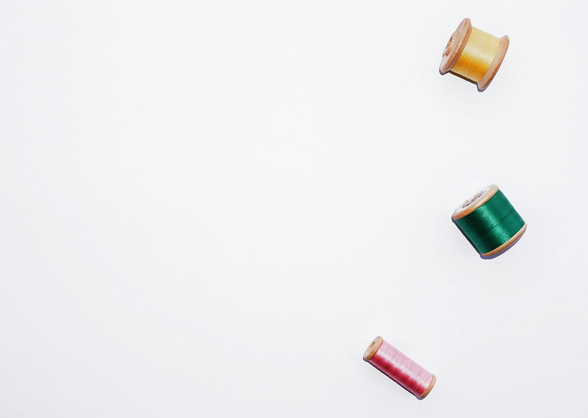 Minimalist flat lay of colorful sewing thread reels on a white background.